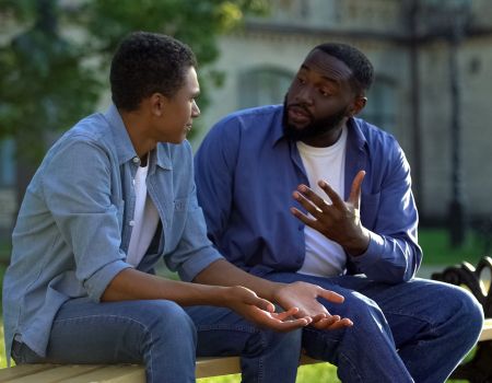 Father arguing teenage son sitting on campus bench, puberty age